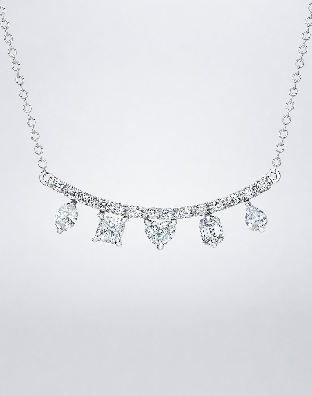 Mindi Mond New York Fancy Cut Necklace in 18K white gold, close view of oval, princess, heart, emerald and pear-cut diamonds hanging from a curved pavé bar