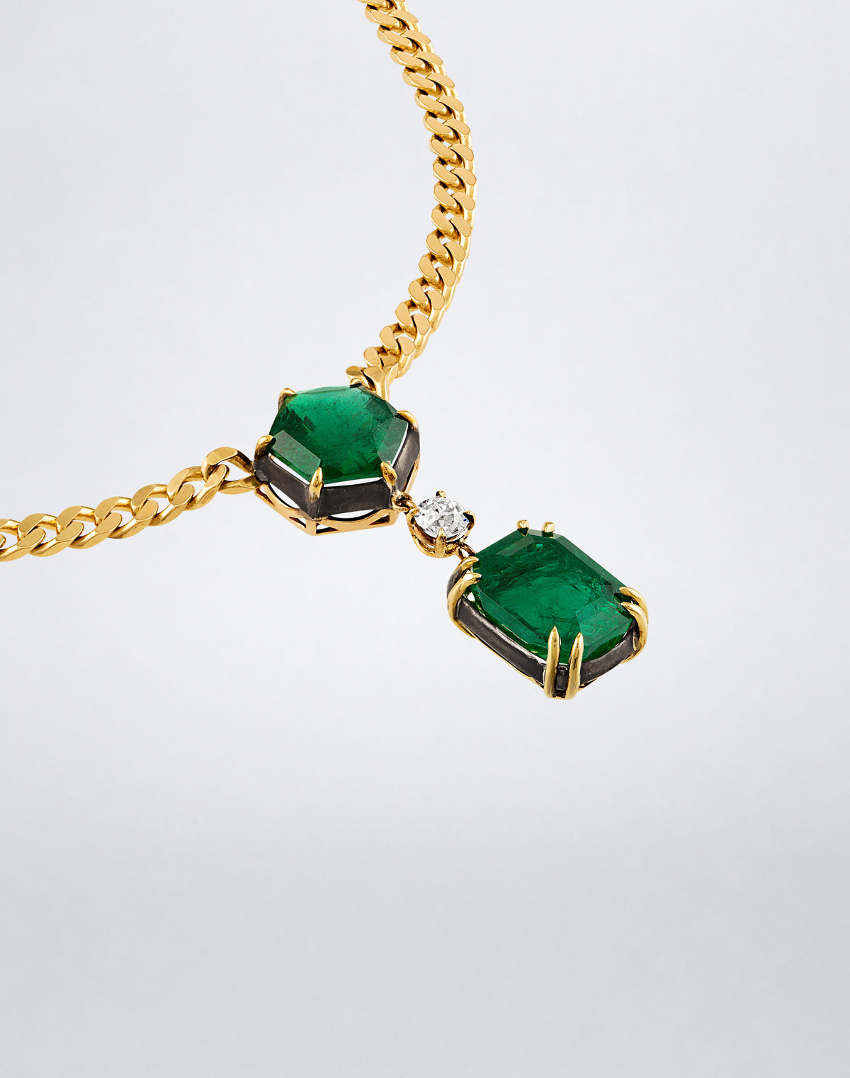 Angled detail of the Mindi Mond New York Dynamic Duo Emerald Necklace showing two emeralds, a diamond accent and yellow gold curb-link chain.
