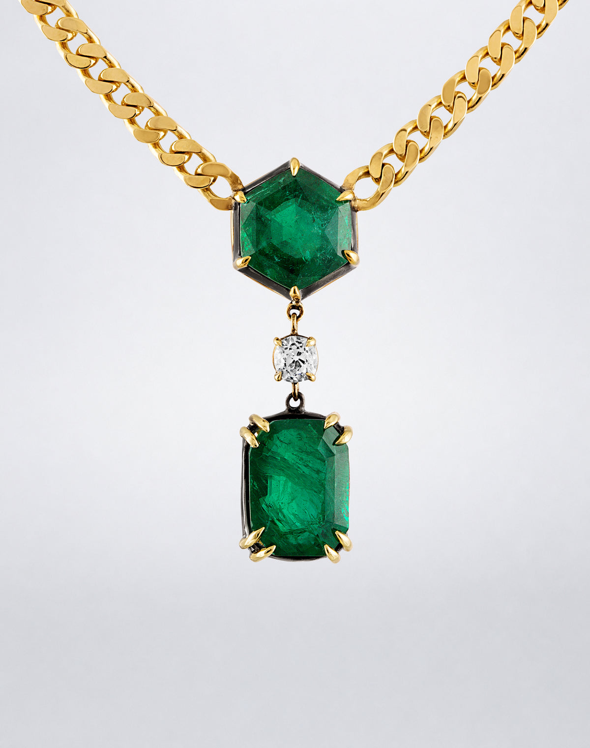 Detail view of the Dynamic Duo Emerald Necklace featuring a hexagonal emerald suspended above an emerald-cut emerald with a diamond between.